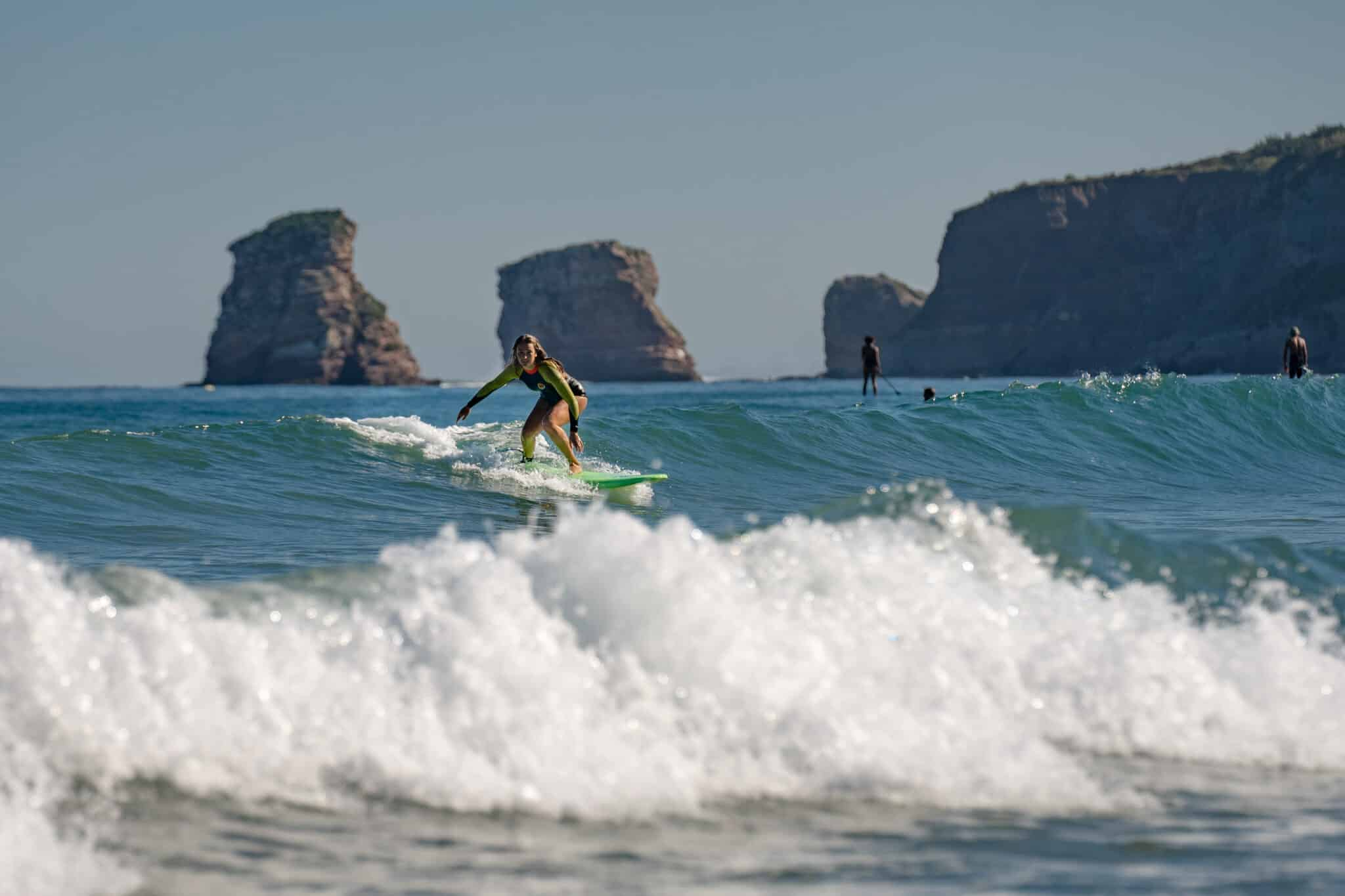Surfista deslizándose sobre una ola en la bahía de Hendaya, con los peñones de Les Deux Jumeaux al fondo